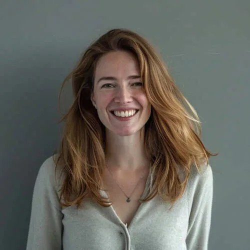 Junge Frau mit langen roten Haaren und grauem Oberteil lächelt vor grauem Hintergrund.