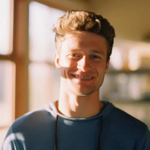 Junger Mann mit lockigem Haar, der in warmem Sonnenlicht lächelt.