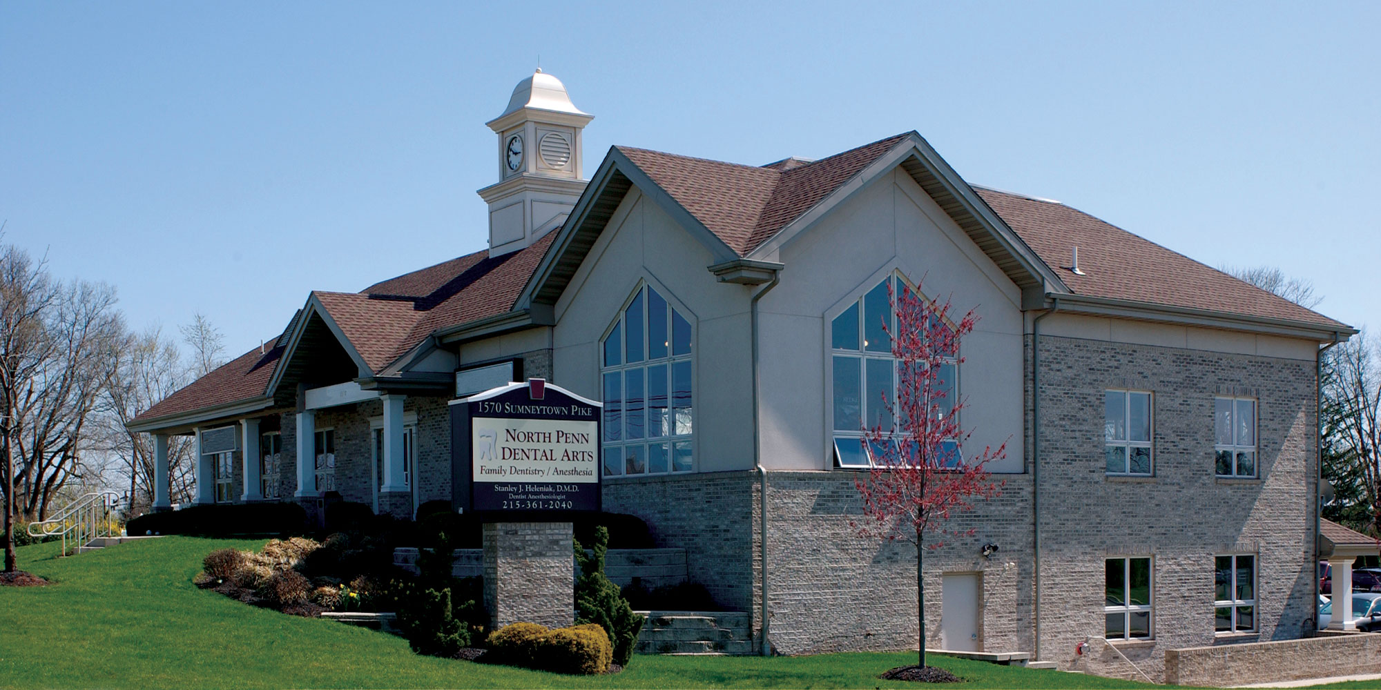 Brick and stucco building with clock tower and sign for North Penn Dental Arts under clear blue sky.