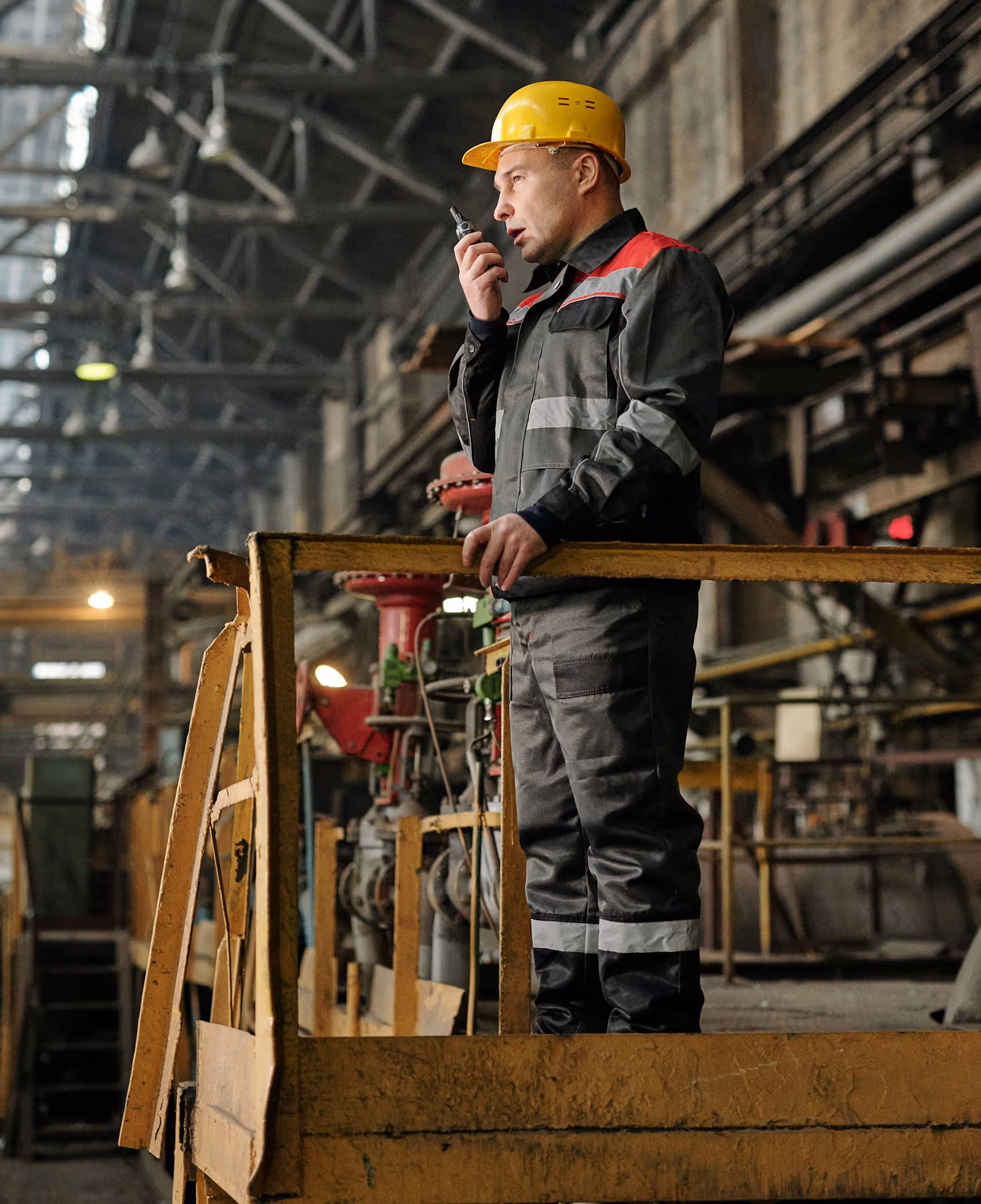 Worker in safety gear speaking into a walkie-talkie inside an industrial facility.