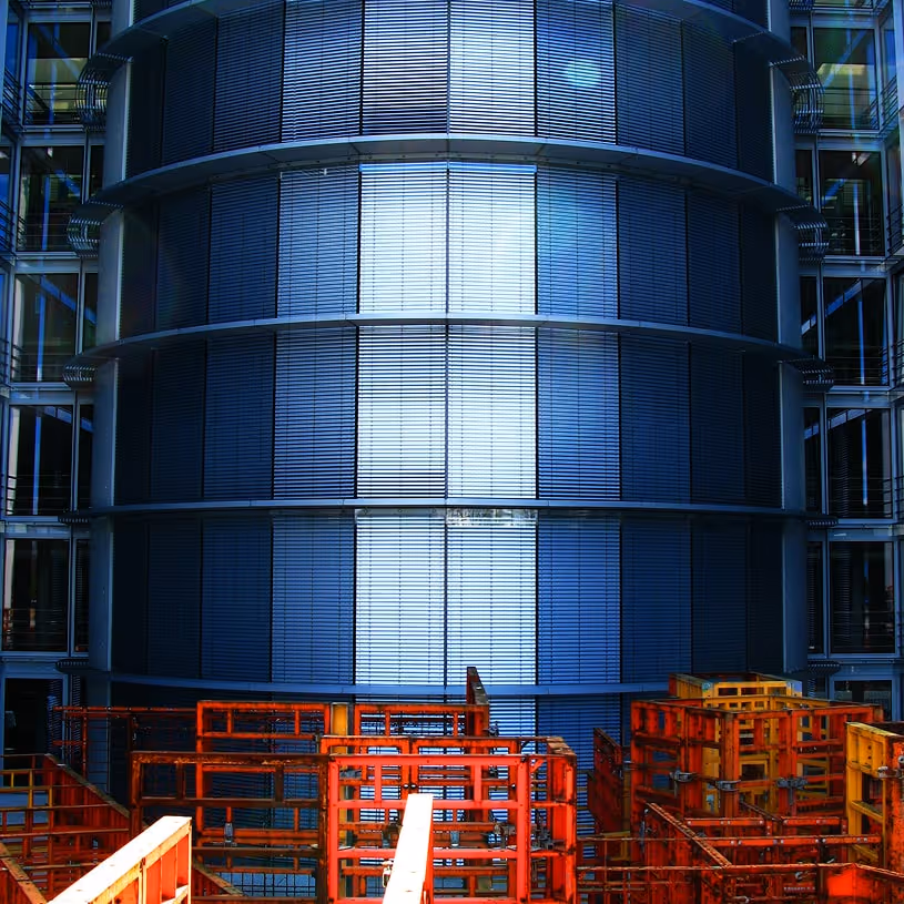 Modern building facade with horizontal blinds and foreground of stacked red metal scaffolding frames.
