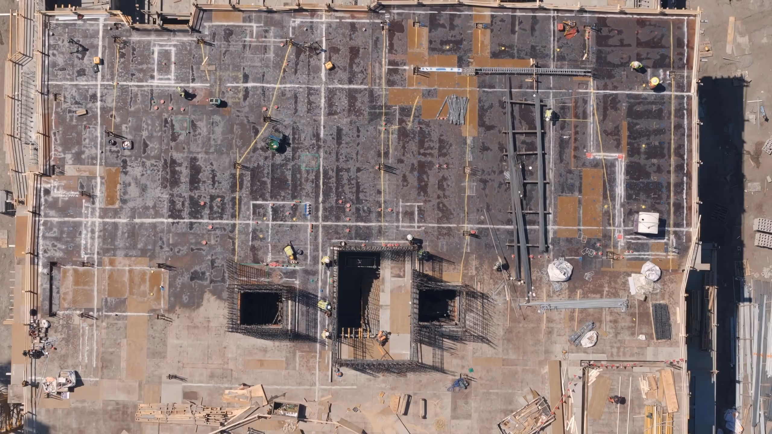 Aerial view of a construction site showing workers, steel reinforcements, and materials on a large concrete slab.