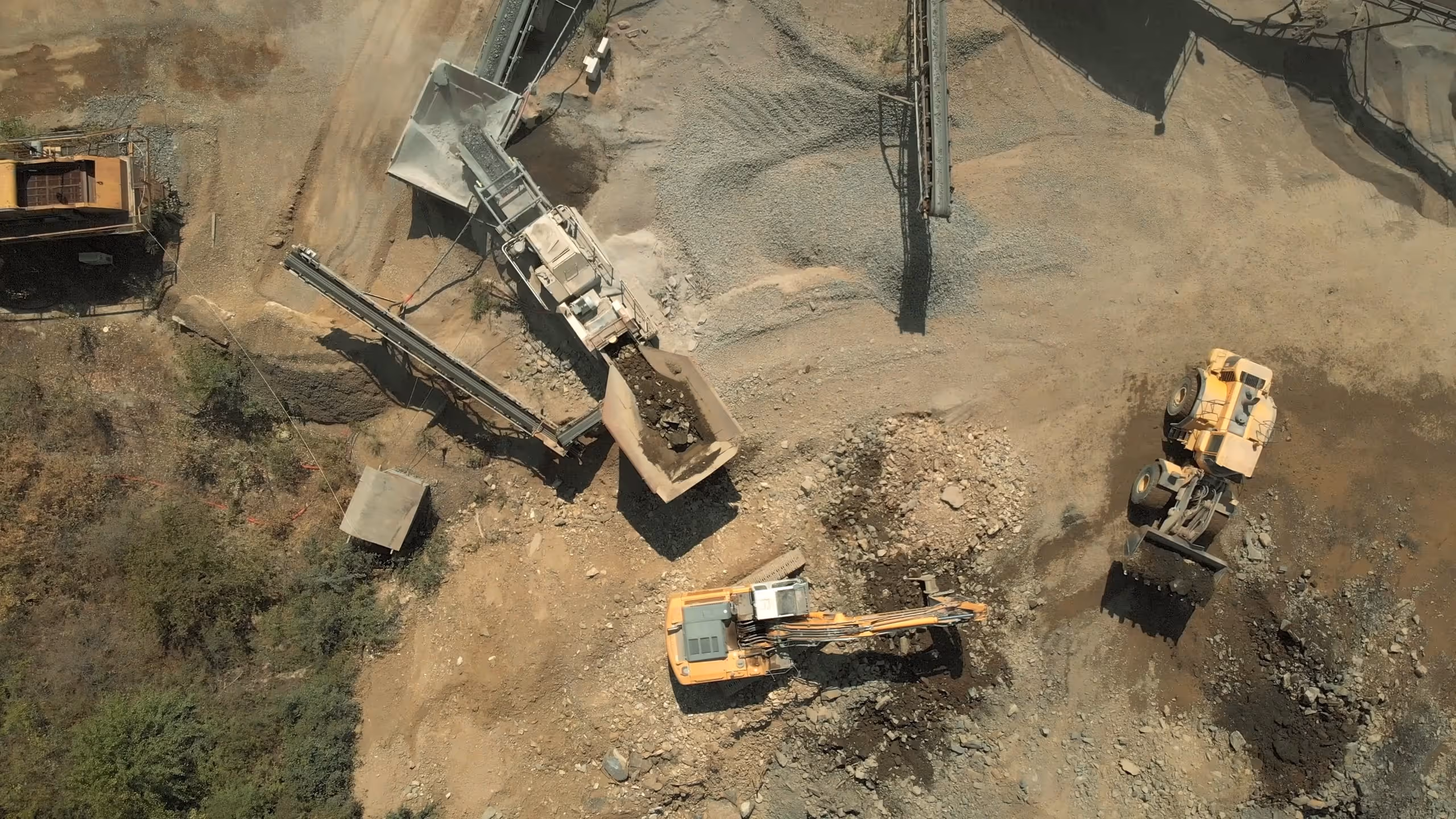 Aerial view of excavation site with large yellow excavator and loader moving dirt and rocks.