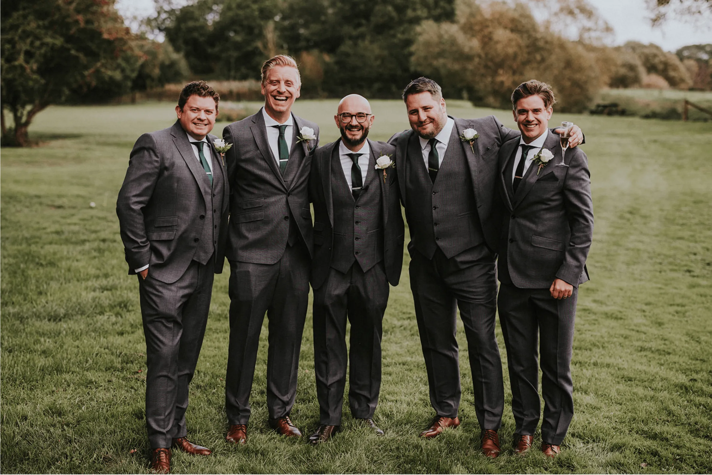 A group of men wearing tailored lounge suits having their photo took in a field.