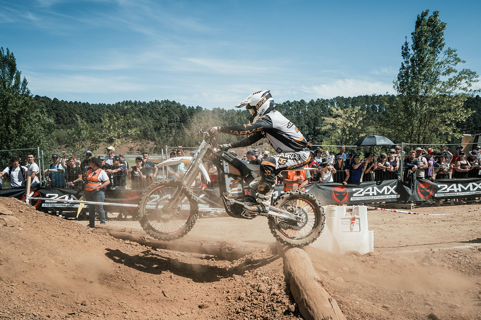 Motorcycle rider in black gear and helmet navigating wooden ramps during an outdoor event with spectators.