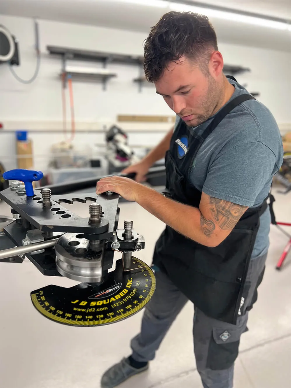 Young man with tattoo on arm operating a JD Squared metal bending machine in a workshop.
