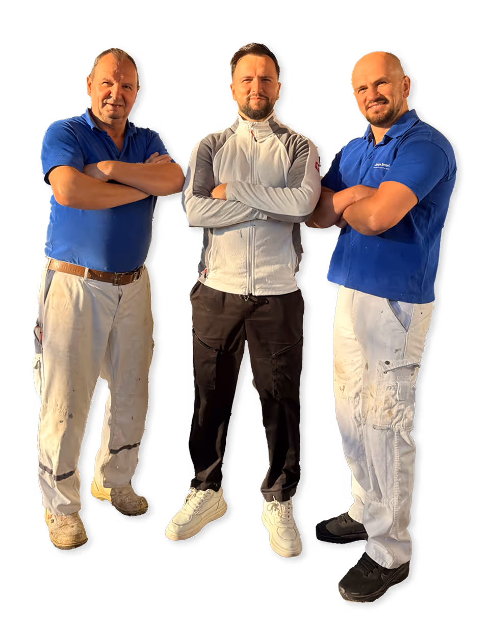 Drei Männer stehen mit verschränkten Armen, zwei tragen blaue Hemden und Arbeitshosen, einer trägt eine weiß-graue Jacke mit schwarzer Hose.