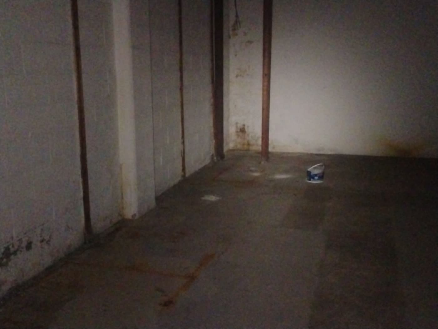 Unfinished basement, painted block walls with yellow-brown mineral staining at the base, steel support posts, bare concrete floor