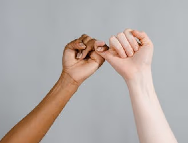 Zwei Hände unterschiedlicher Hautfarbe, die sich mit verschlungenen kleinen Fingern versprechen.
