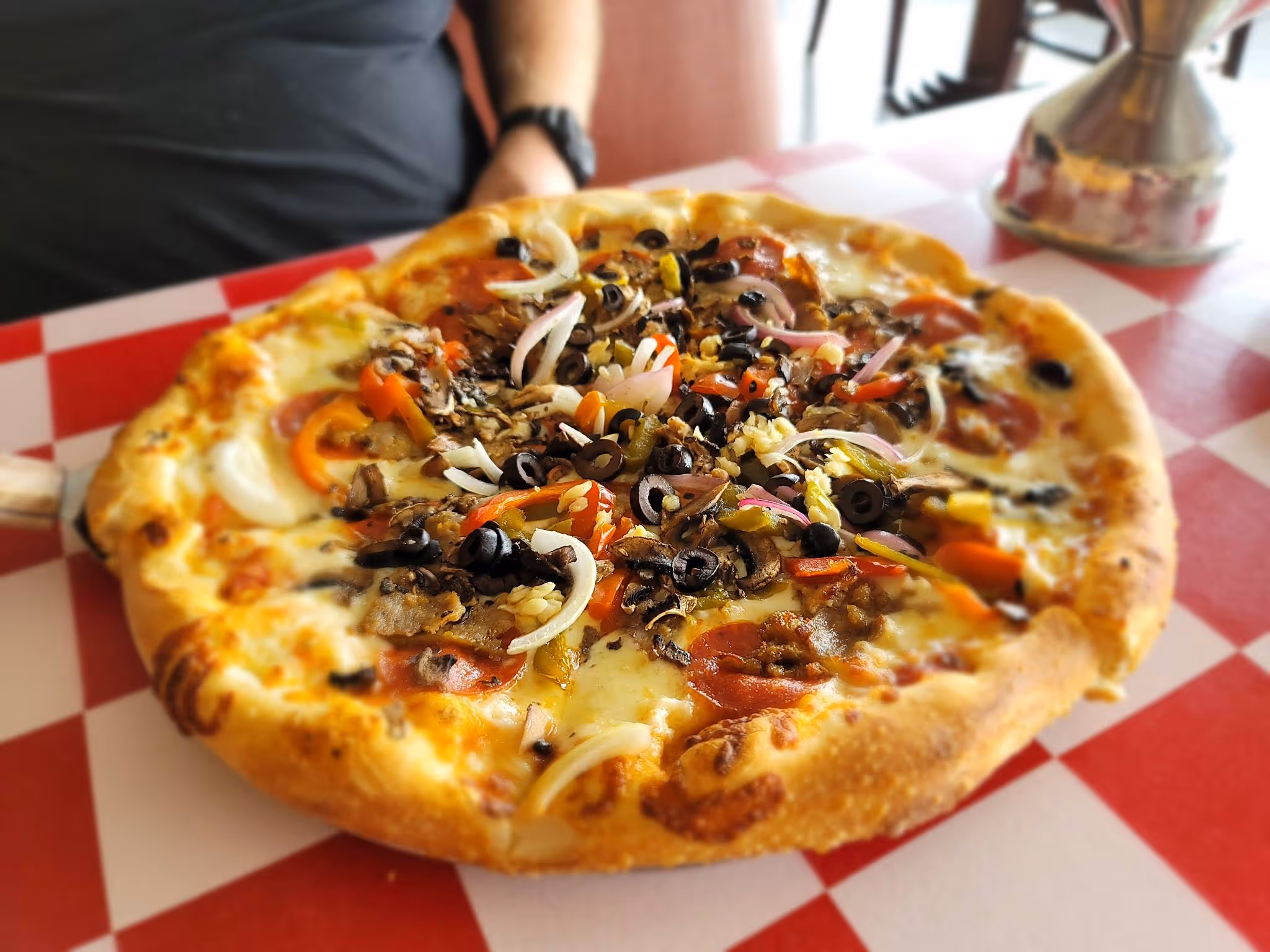 A pizza with pepperoni and mushrooms on a red and white checkered tablecloth.