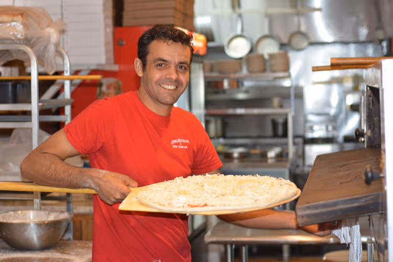 A man holding a pizza in a kitchen.