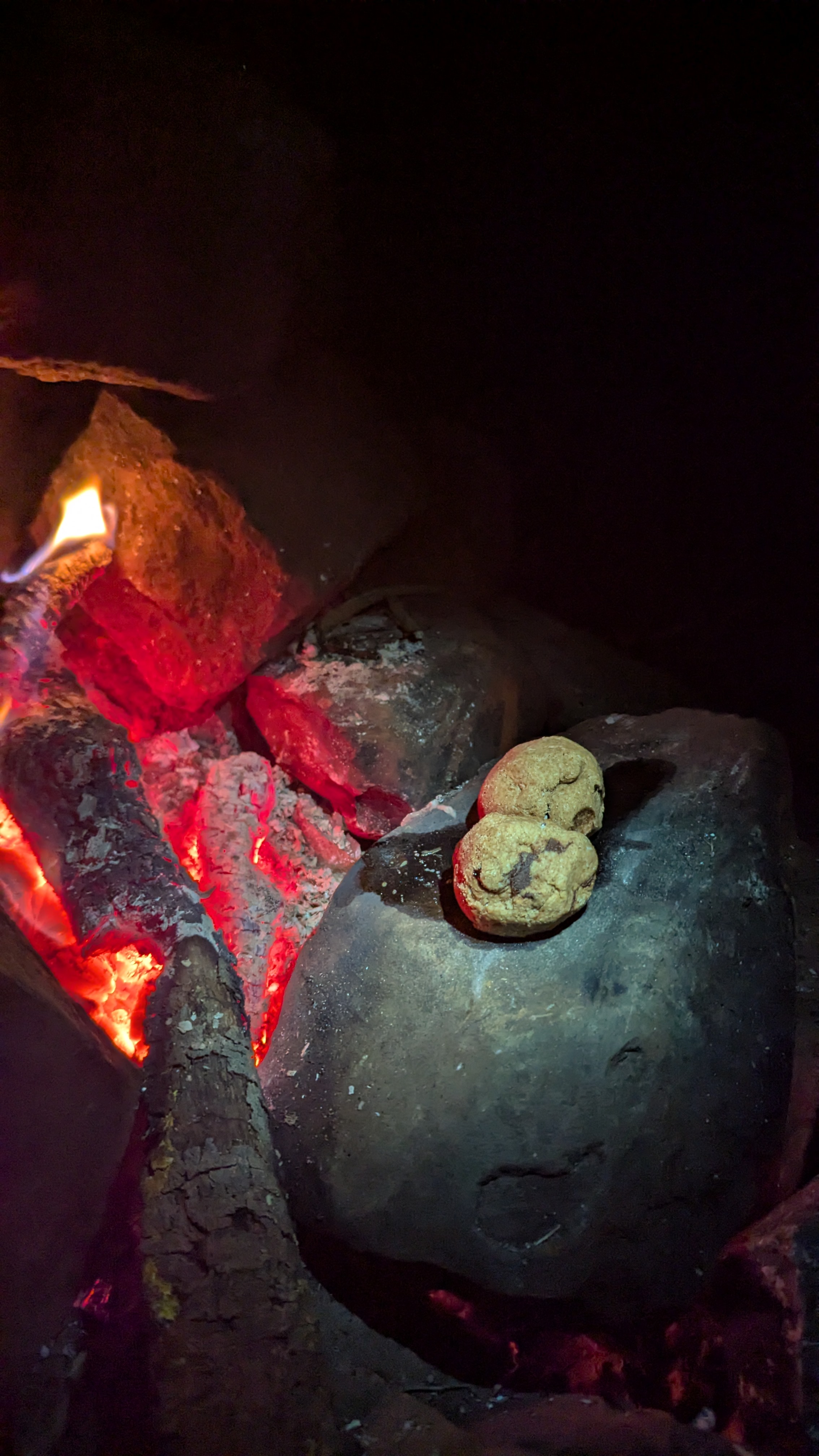 Zwei Kekse auf einem Stein neben glühenden Holzstücken in einem Lagerfeuer.