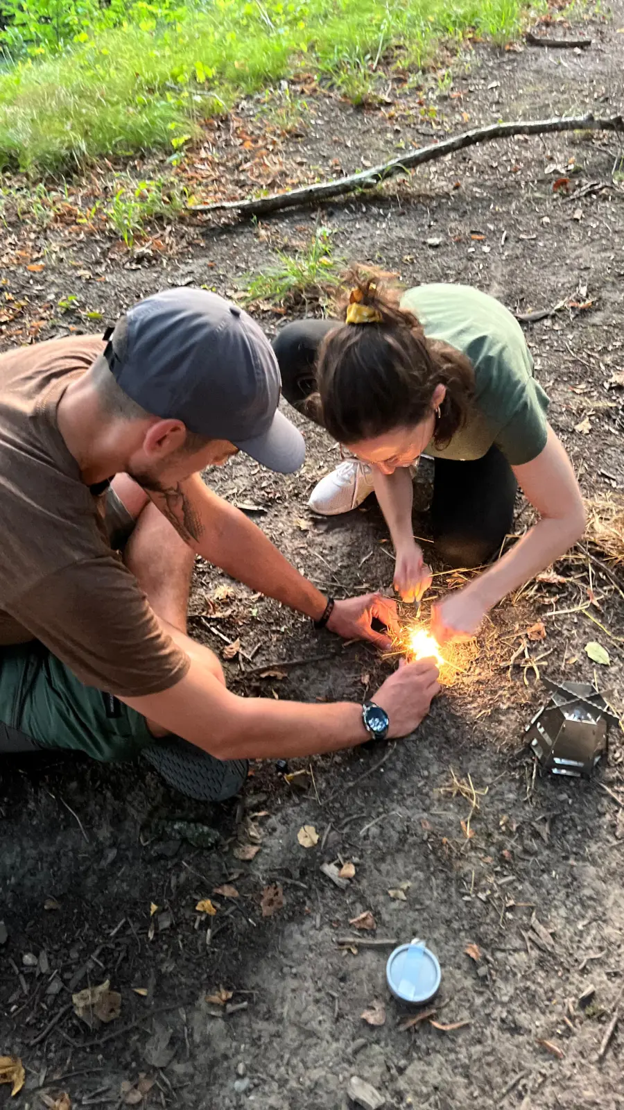 Zwei Personen knien im Wald und zünden ein Feuer mit Funken an.