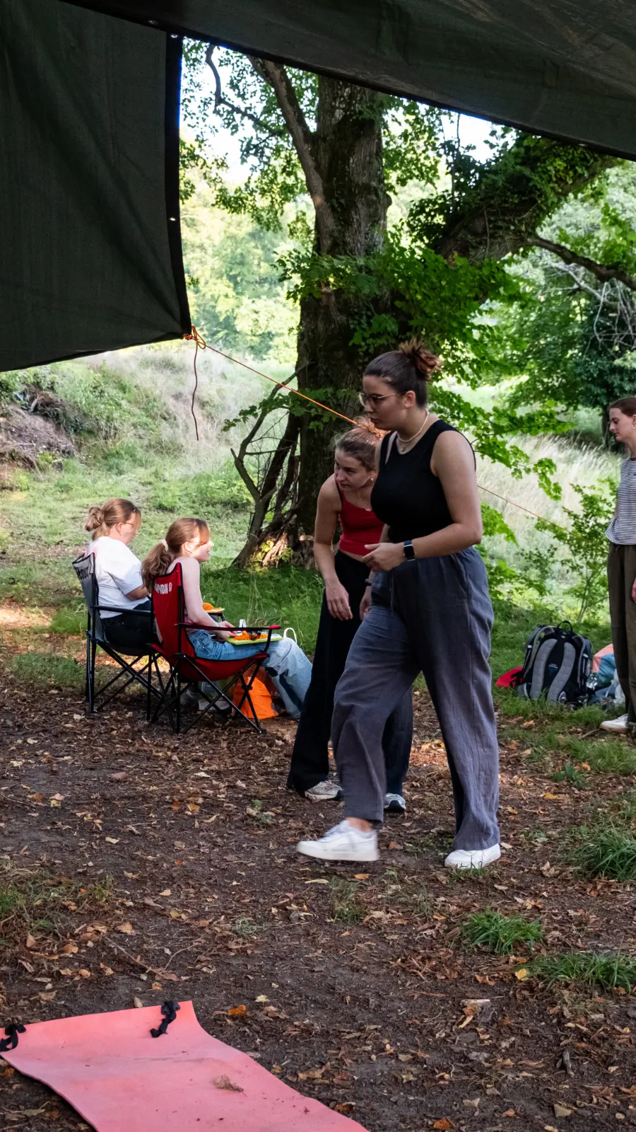 Gruppe junger Frauen und Mädchen bei Outdoor-Aktivitäten unter einem Zelt im Wald.