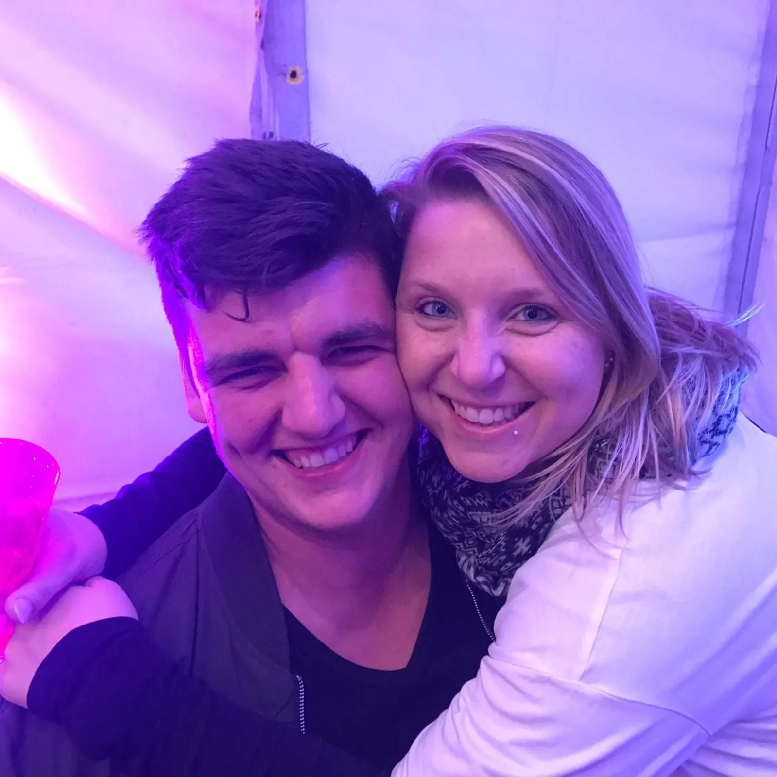 Junges Paar umarmt sich lächelnd in lila beleuchtetem Raum.