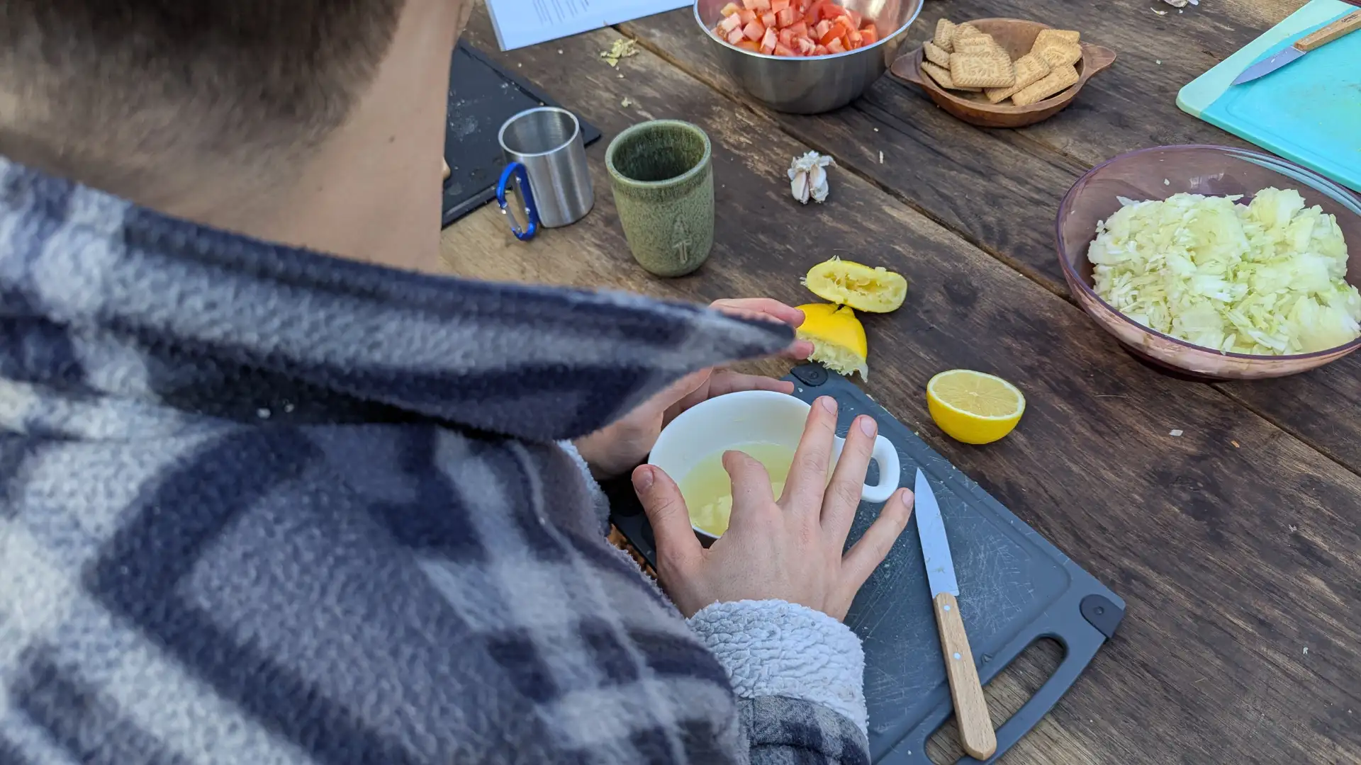 Person presst Zitronensaft in eine Tasse auf einem Holztisch mit geschnittenem Gemüse und Keksen.