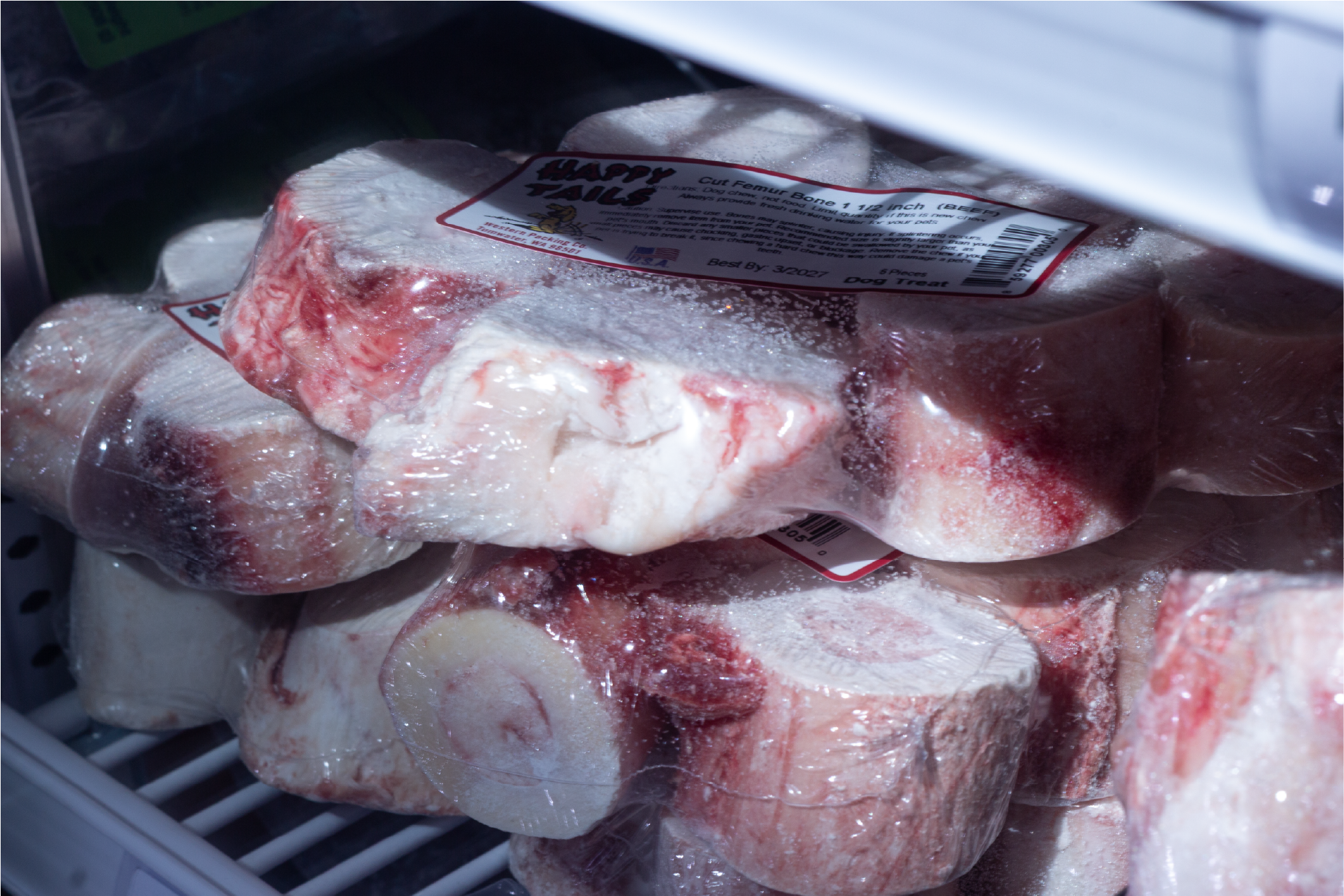 Packages of raw meat sit in a freezer, they are lit by sunlight coming through the freezer door