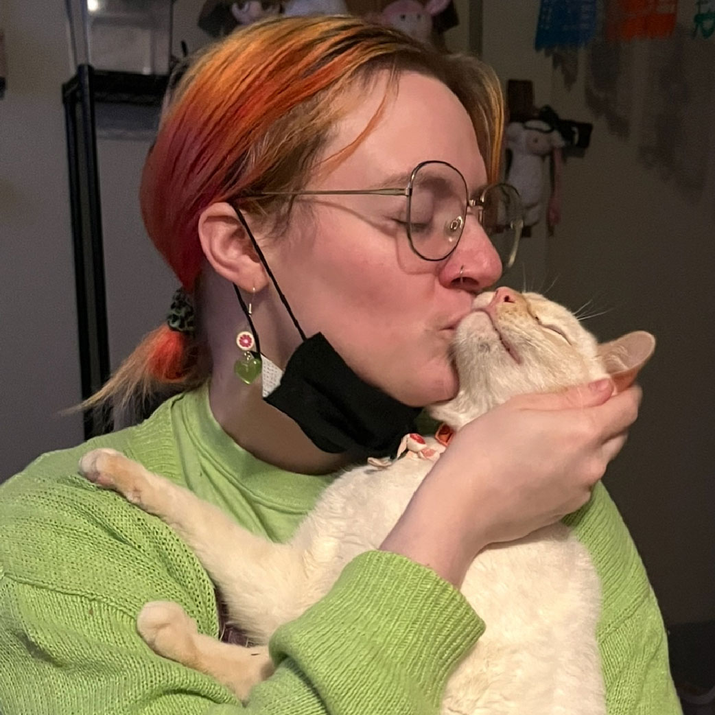 Jeff is wearing a green sweater embracing and kissing their beige cat