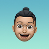 3D emoji face of a smiling person with glasses and a black bun hairstyle on a gradient blue background.