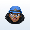 3D emoji of a smiling person with curly black hair, glasses, and a blue cap.