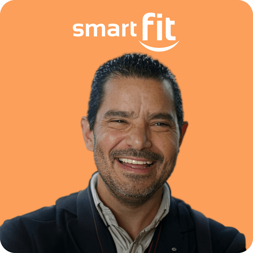 Smiling man with short dark hair and beard wearing a dark jacket against an orange background with the smart fit logo above.