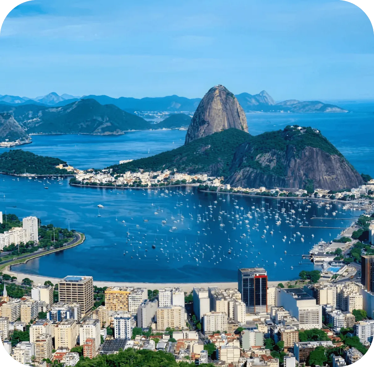 Cityscape with bay filled with boats and two large rocky hills covered in green vegetation.