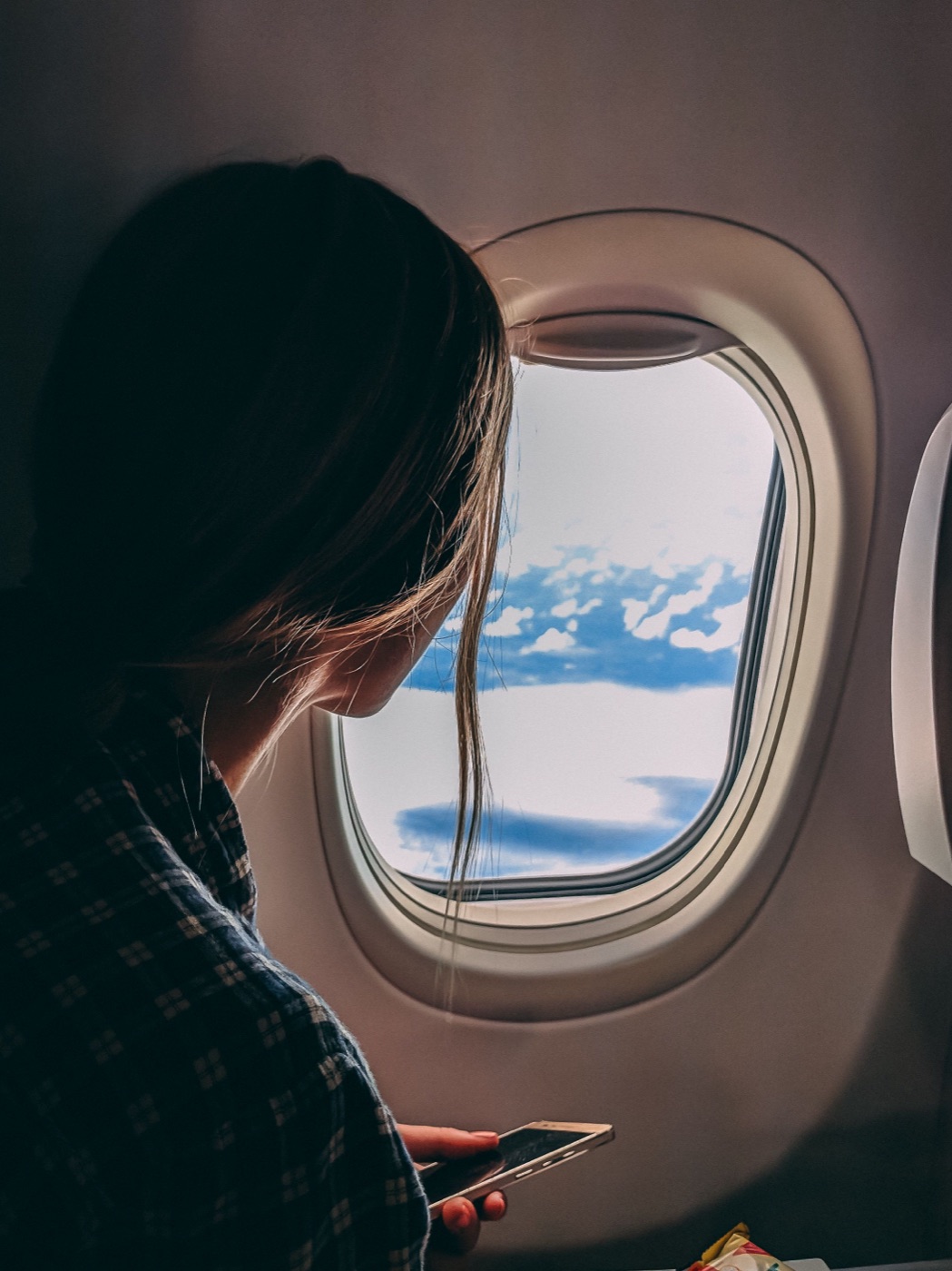 Traveler looking out an airplane window while holding a Clara TravelPay virtual card