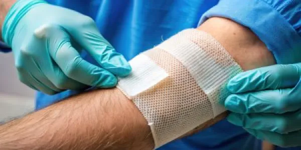 Healthcare professional wearing blue gloves applying a bandage to a patient's forearm wound.