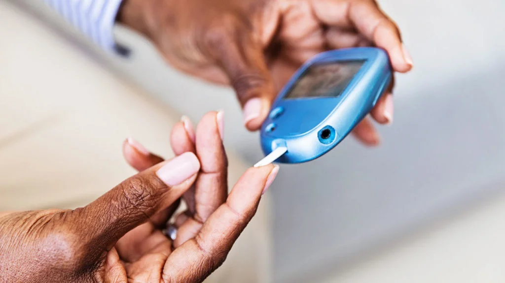 Person holding a blue blood glucose meter and placing a test strip on their fingertip for diabetes testing.