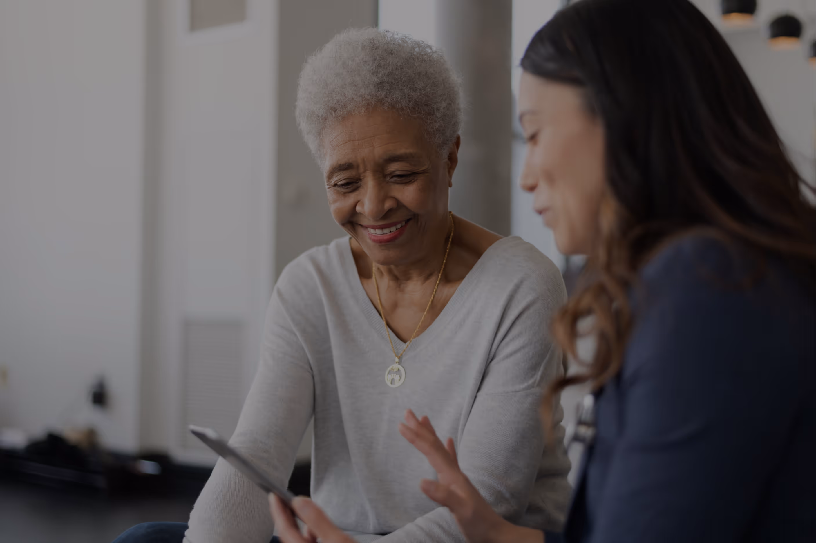Smiling elderly woman looking at a smartphone held by a younger woman during a conversation.