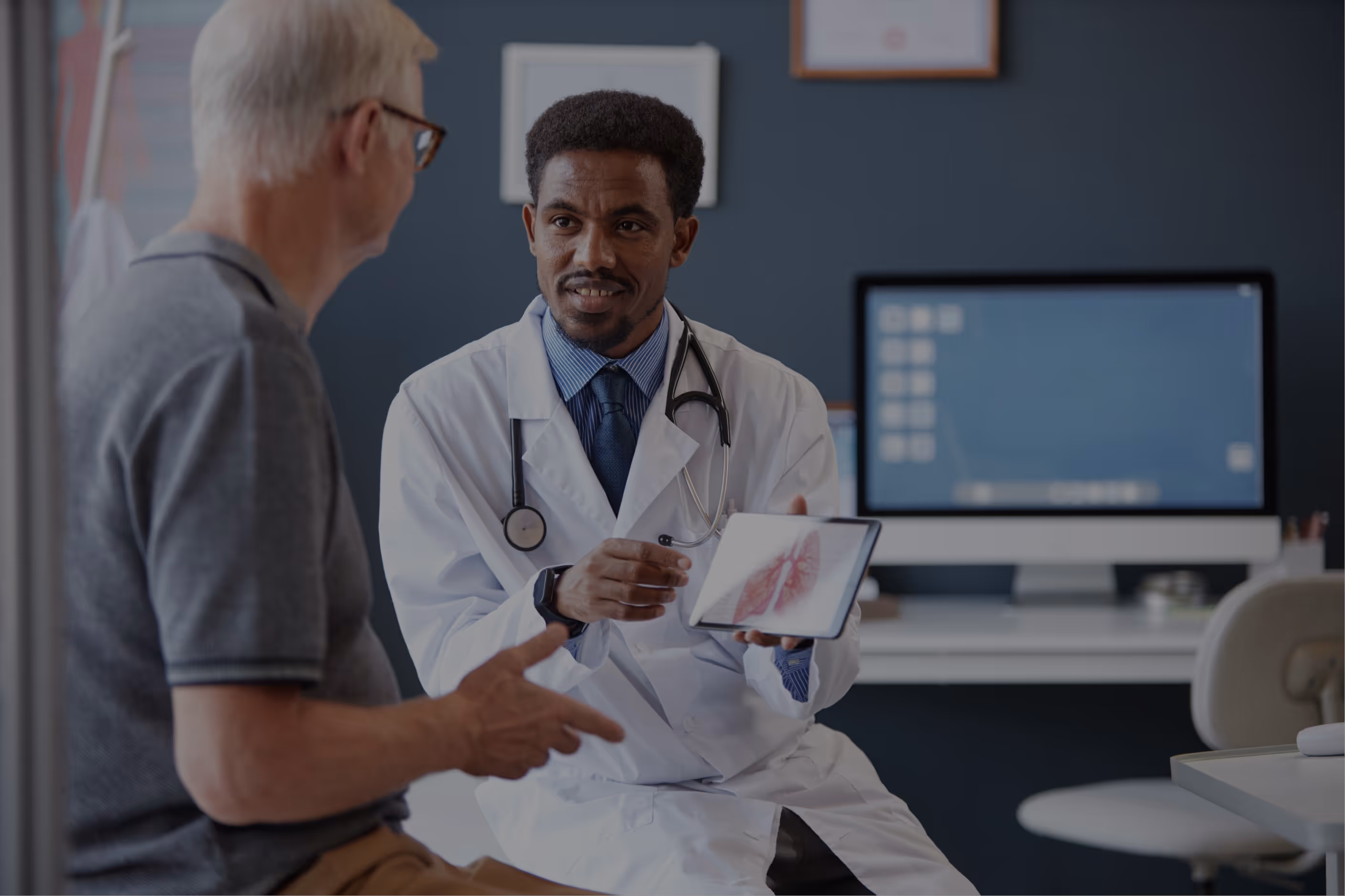 Doctor in a white coat showing a tablet with a lung image to a senior patient in a medical office.