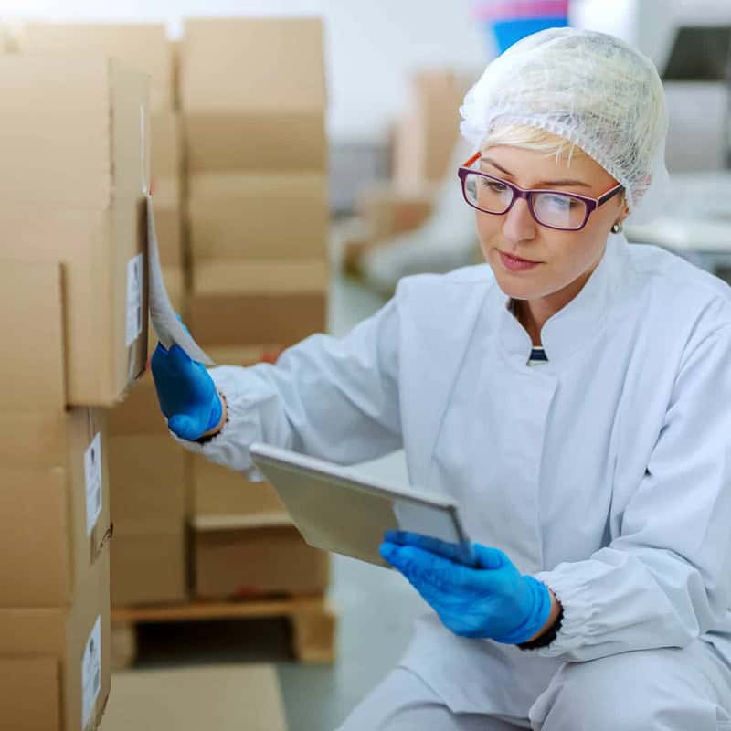 Quality control inspector in a lab coat checking packaged goods with a tablet