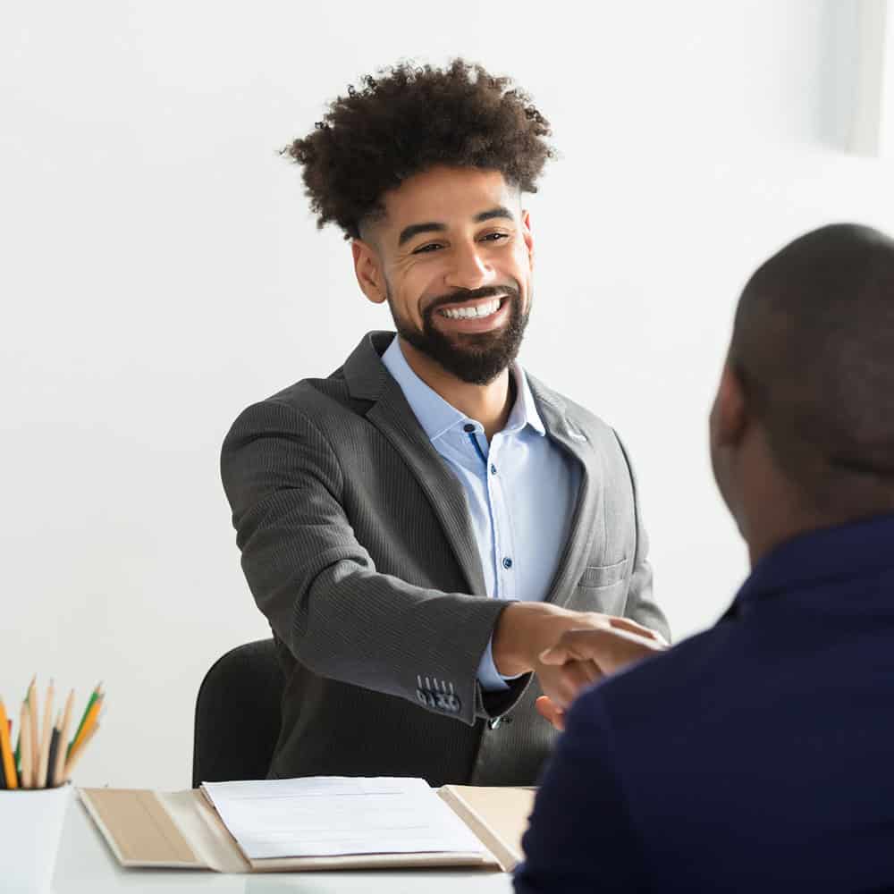 Smiling job candidate shaking hands with an interviewer across an office desk