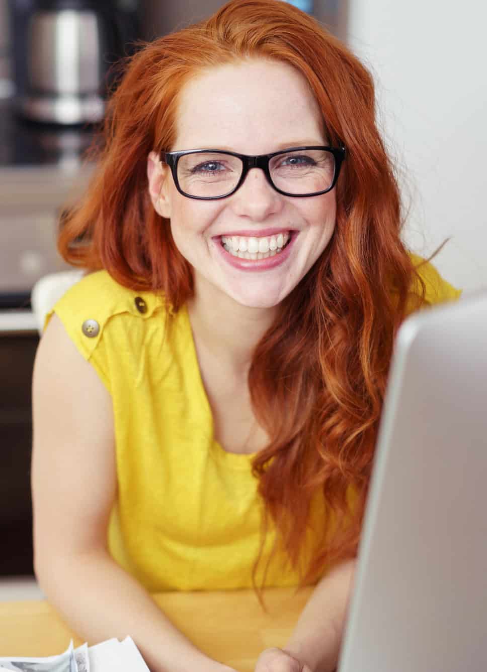 Cheerful young woman in glasses smiling while using a laptop at home