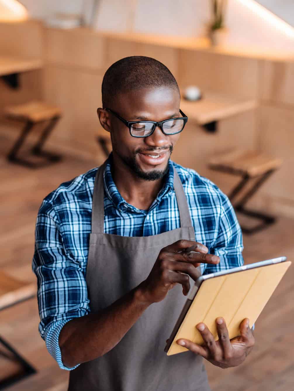 Smiling cafe worker in an apron using a tablet in a restaurant