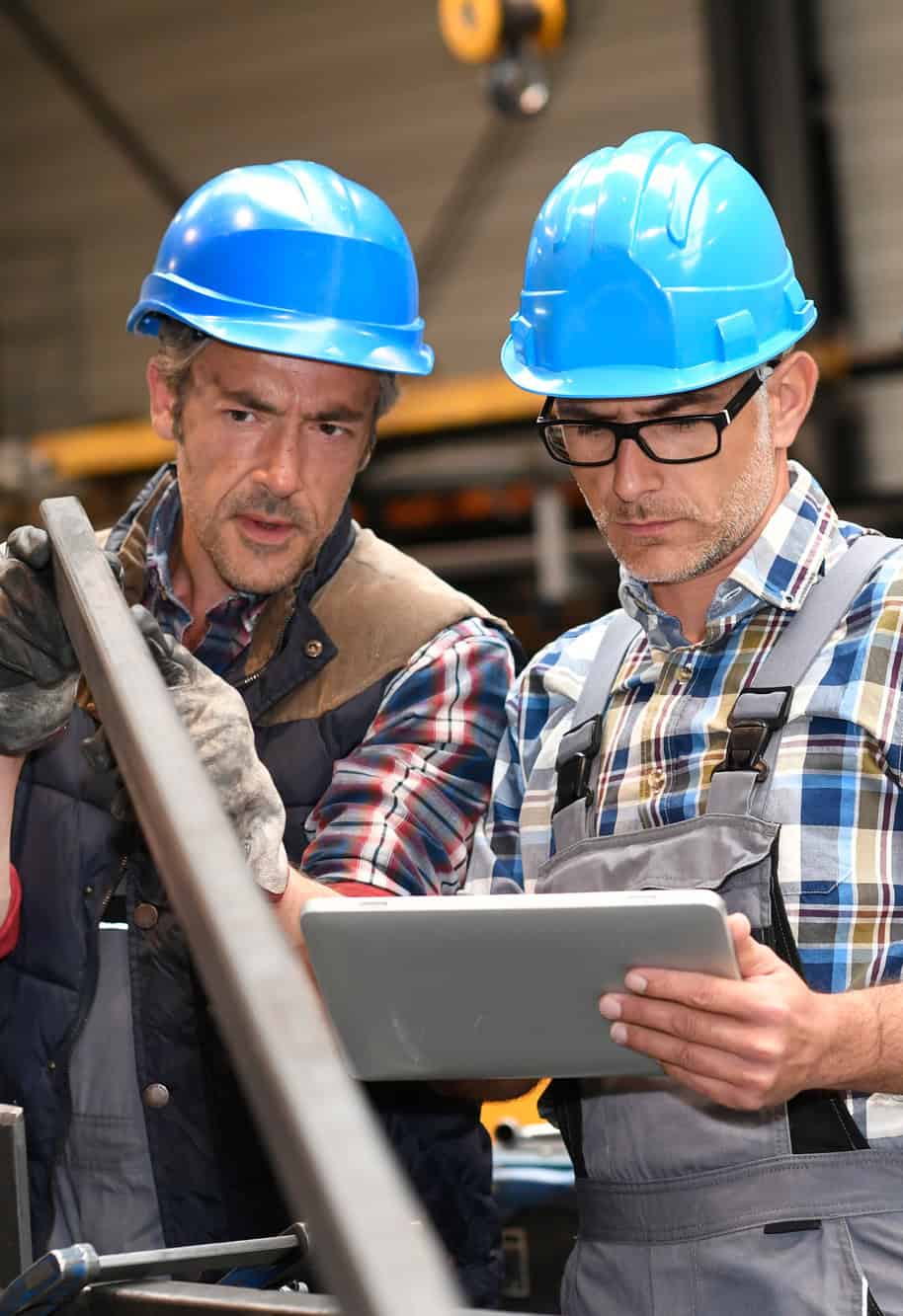 Two industrial workers in hard hats reviewing a tablet together on a factory floor