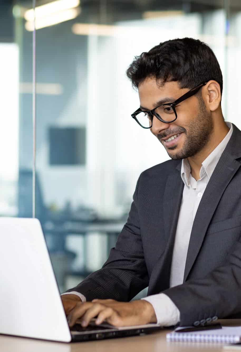 Smiling businessman in a suit and glasses working on a laptop in a modern office