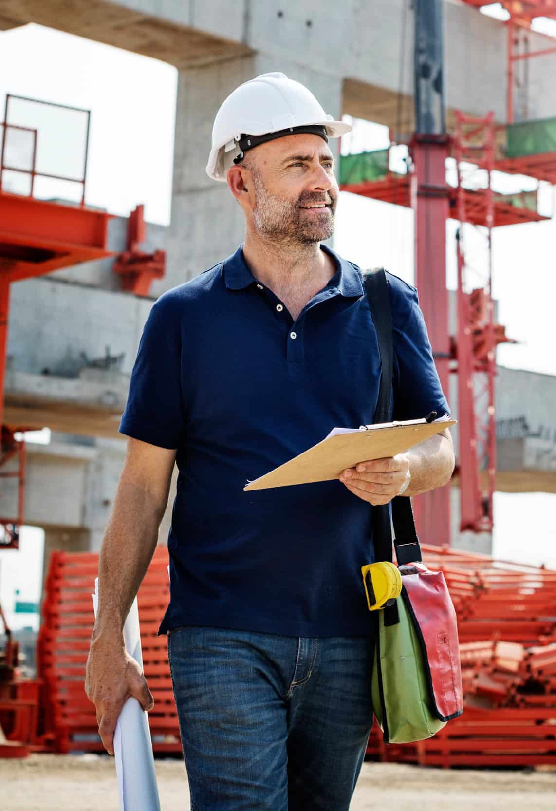 Construction site supervisor in a hard hat holding a clipboard and blueprints at a building site