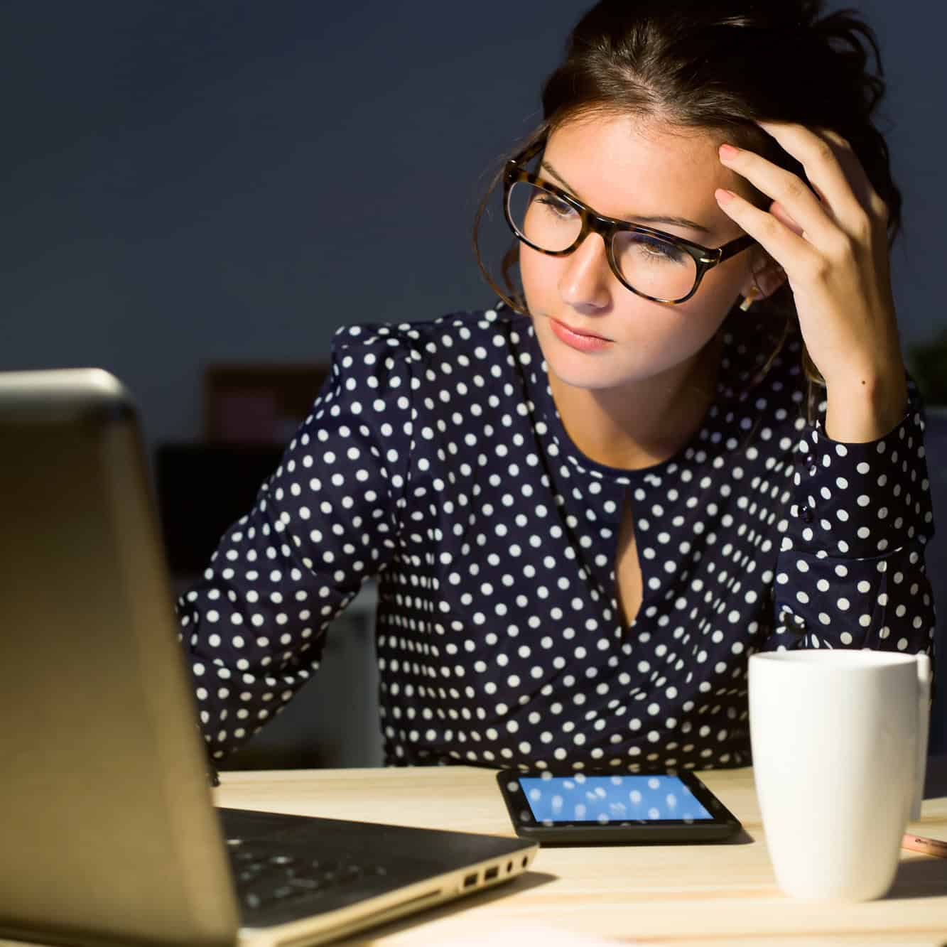 Tired job seeker resting her head on her hand while searching for work on a laptop at night