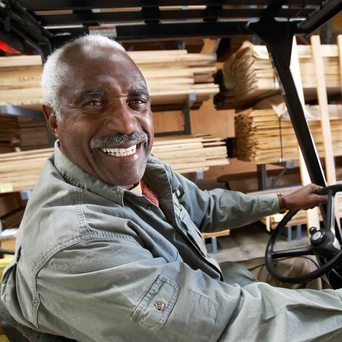 Smiling senior forklift driver at the wheel in a lumber warehouse