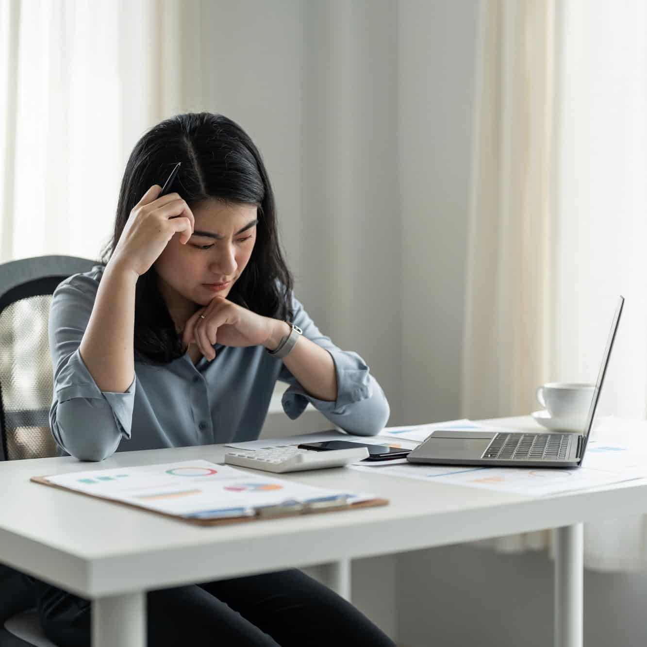 Stressed manager resting her head on her hand while reviewing paperwork at her desk