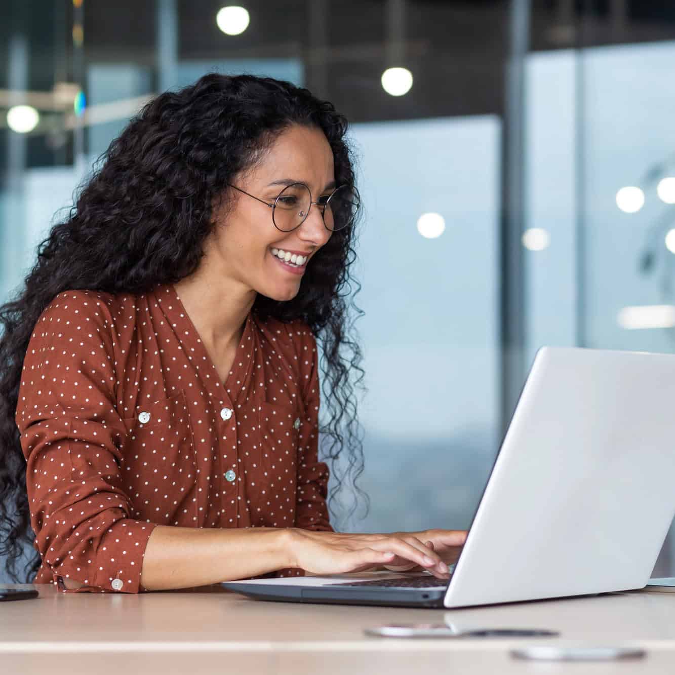 Smiling professional woman in glasses working on a laptop in a modern office