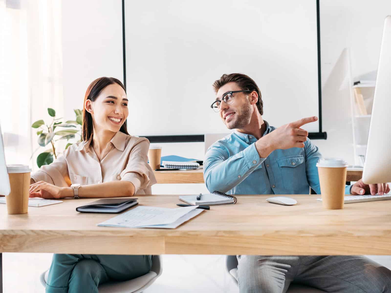 Two office coworkers collaborating at a computer in a bright modern workspace