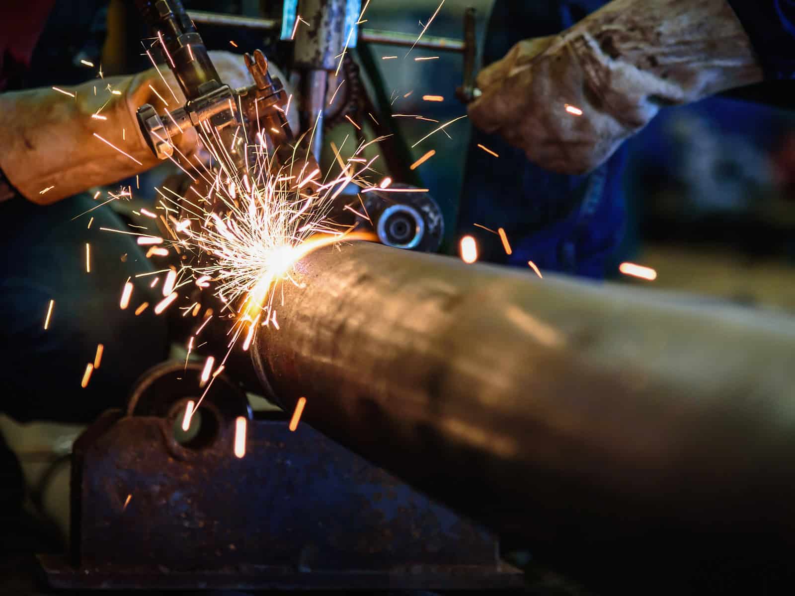 Skilled tradesworker grinding a metal pipe with sparks flying in a fabrication shop