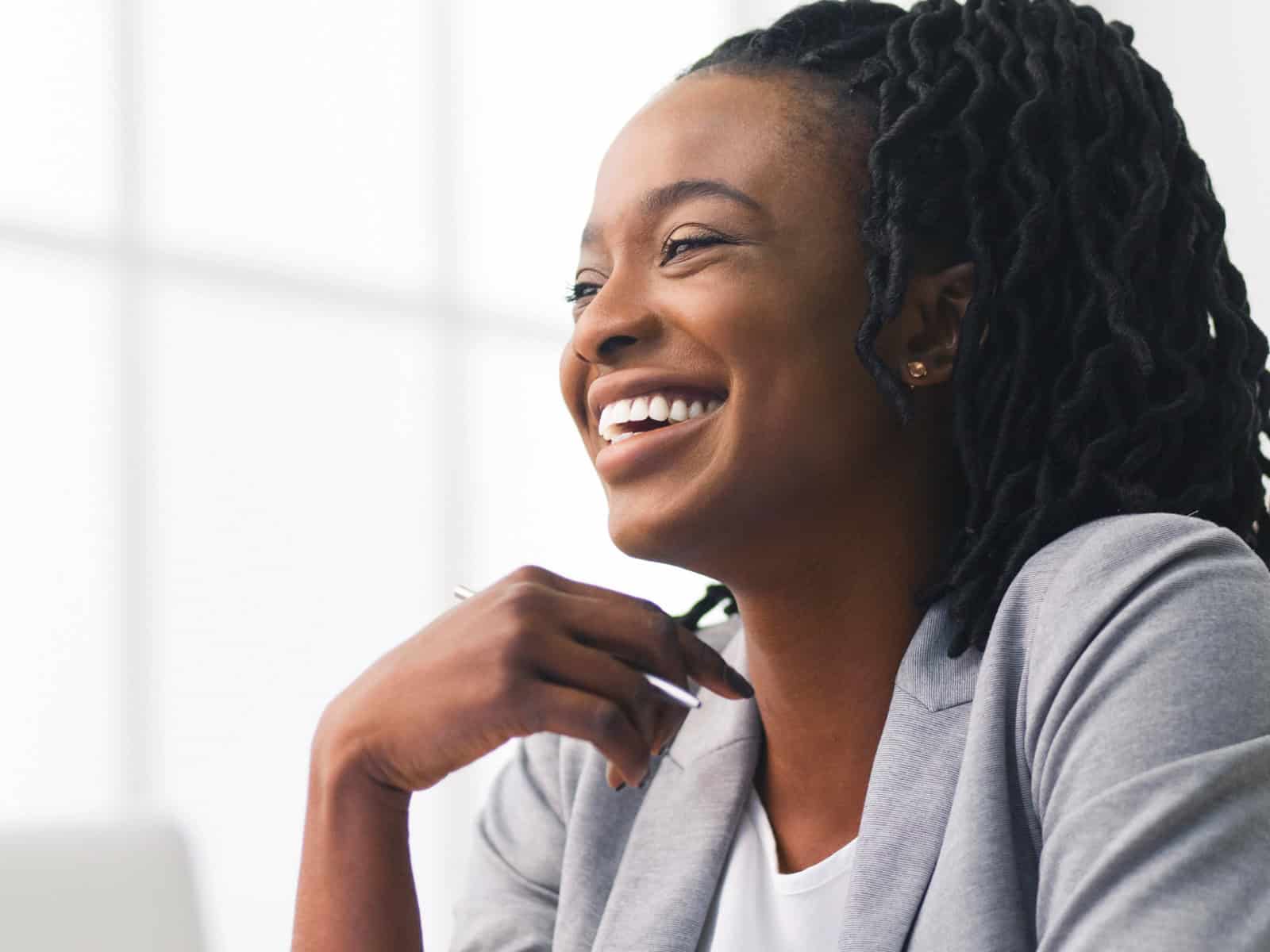 Smiling professional woman in a blazer holding a pen in a bright office