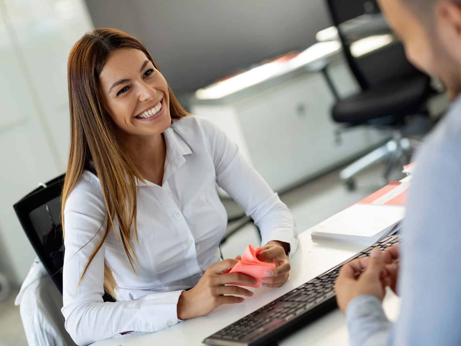 Smiling administrative worker at an office desk during a meeting with a colleague