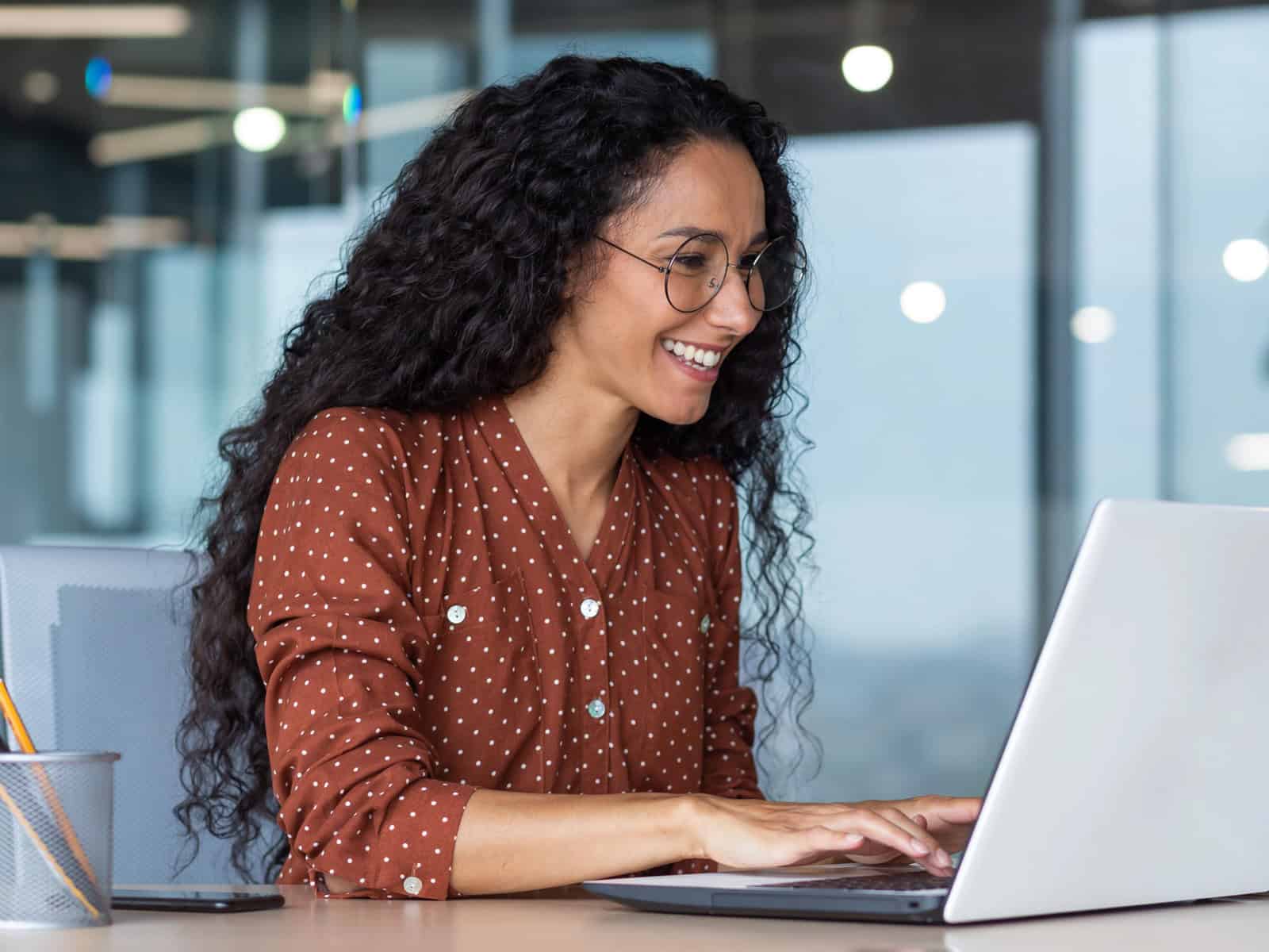 Smiling professional woman in glasses working on a laptop in a modern office
