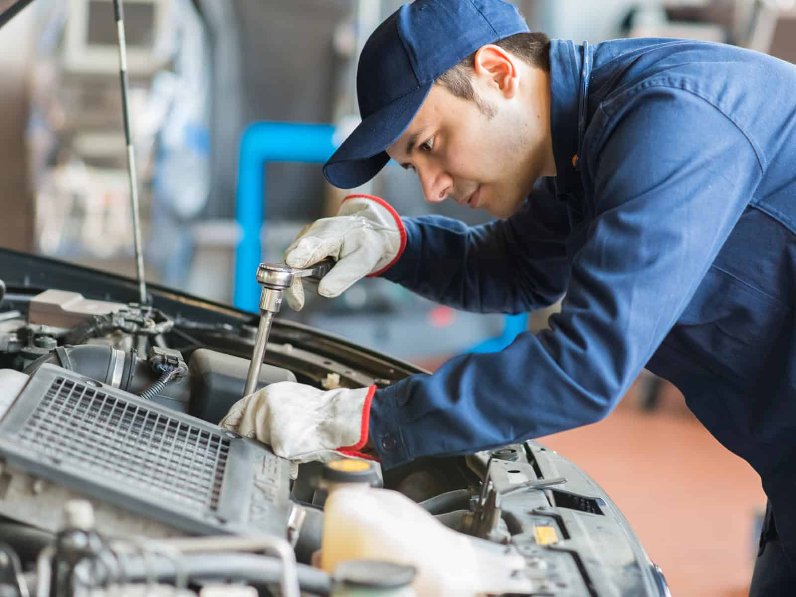 Automotive mechanic in uniform using a wrench to repair a car engine