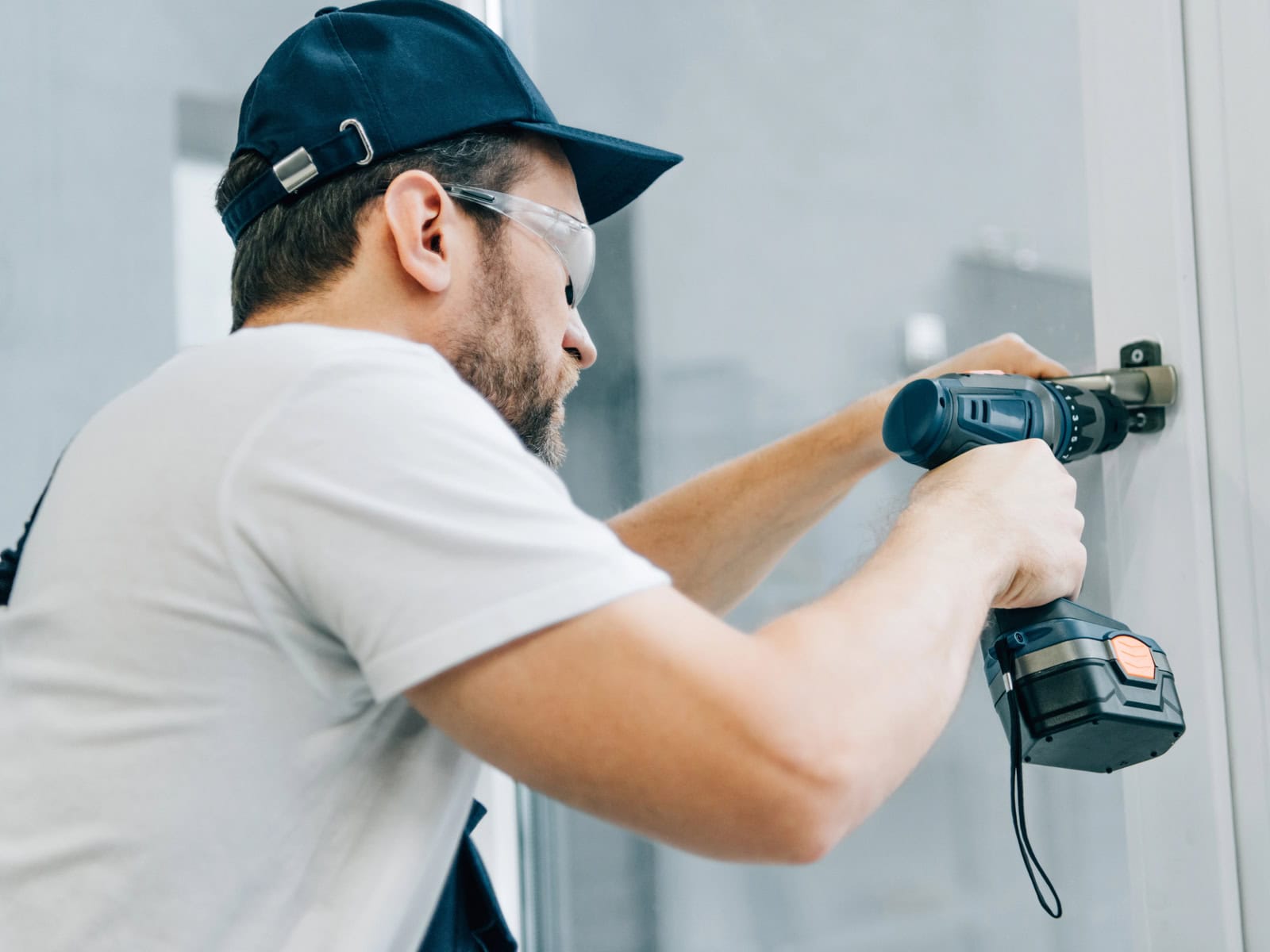 Tradesman in safety glasses using a cordless drill to install hardware on a wall