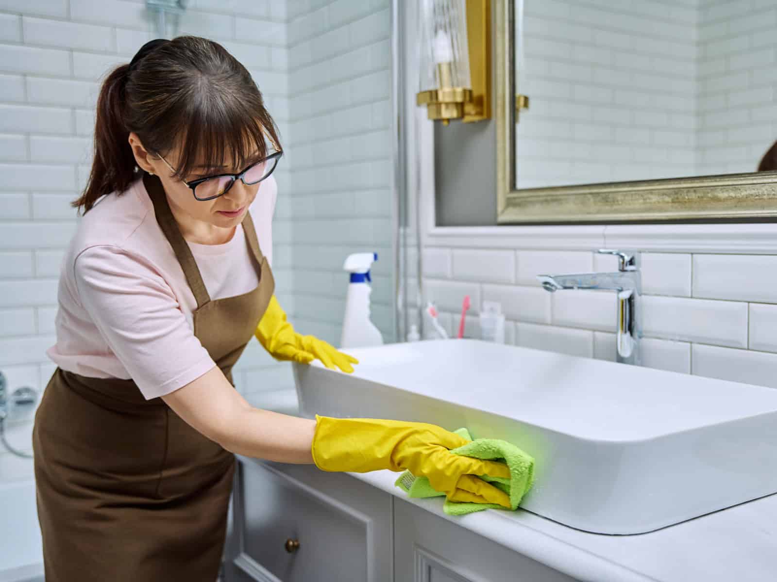 Cleaning staff member in gloves wiping down a bathroom sink and vanity
